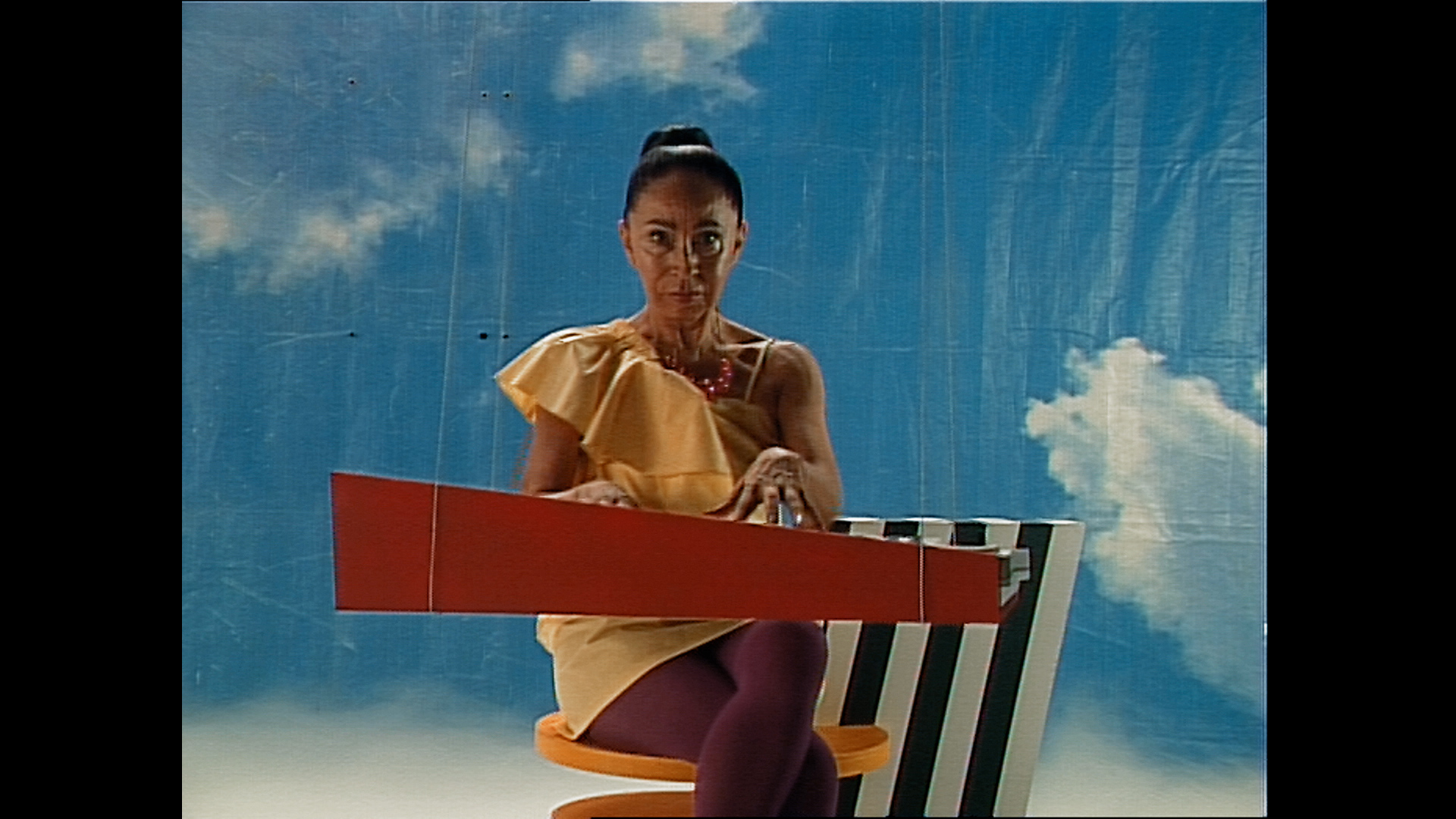 An older woman staring into the camera while playing the piano.