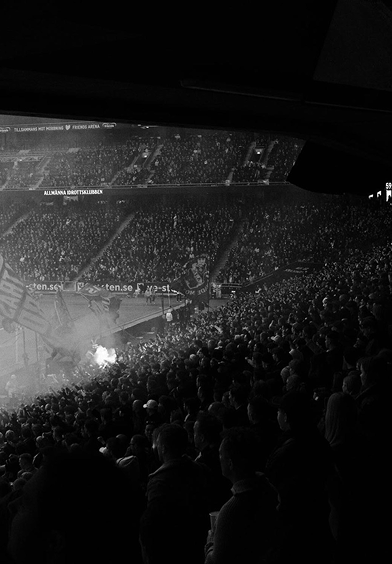 A crowded stand at a football stadium veiled in smoke.